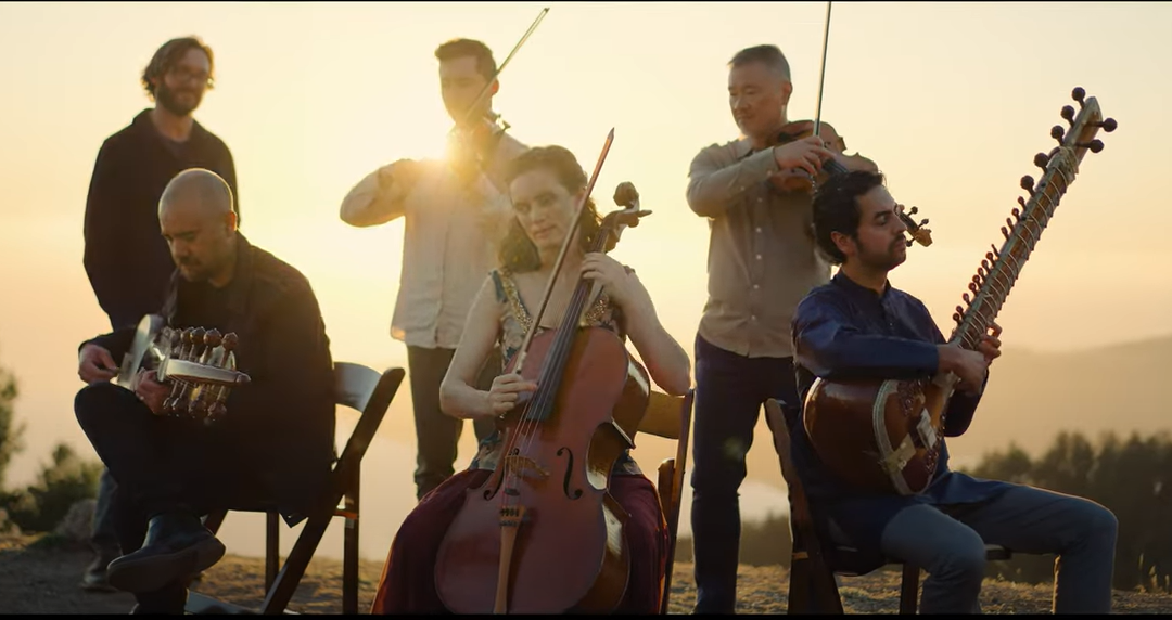 six musicians playing instruments with the sun setting behind them